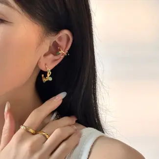 Woman wearing LIVKE gold vine earrings with green gemstones at outdoor garden party, showcasing organic luxury jewelry