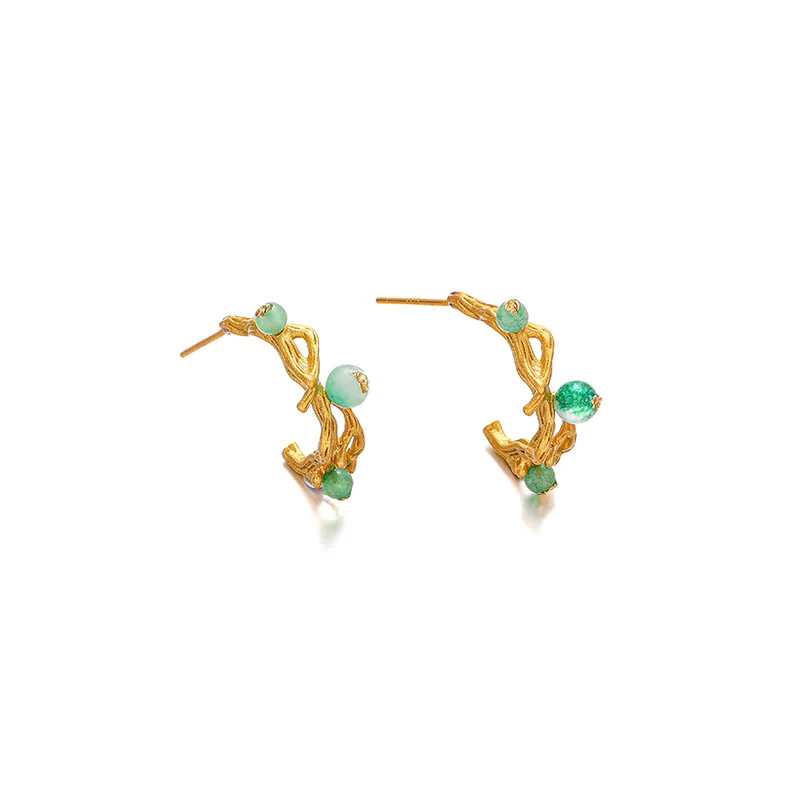 Woman wearing LIVKE gold vine earrings with green gemstones at outdoor garden party, showcasing organic luxury jewelry