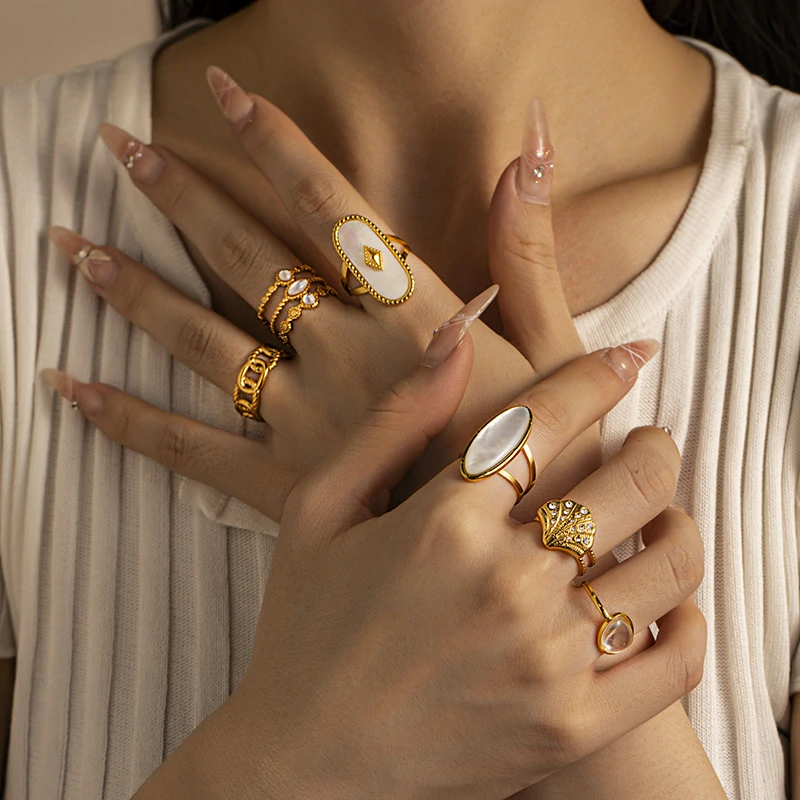 Tanned hand wearing LIVKE shell ring layered with thin gold bands against ocean waves