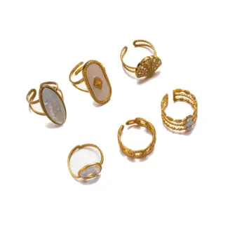 Tanned hand wearing LIVKE shell ring layered with thin gold bands against ocean waves