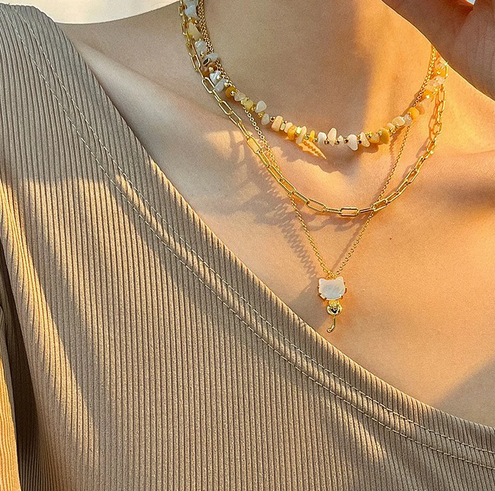 Woman wearing LIVKE cat and shell necklace walking with cat on sunset beach, symbolizing pet love and coastal aesthetic jewelry