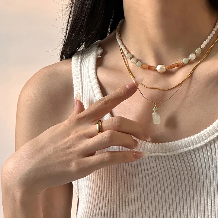 Woman wearing LIVKE green aventurine and white jade necklace with cashmere sweater, showcasing minimalist jewelry for urban elegance