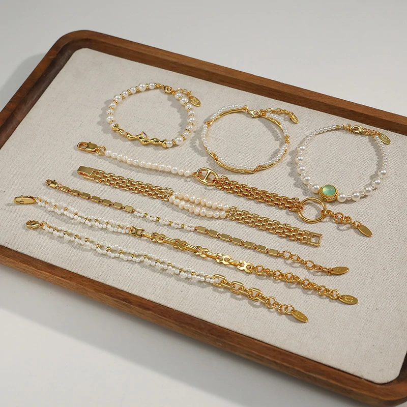 Stylist mixing LIVKE gold chain modules with baroque pearls on antique velvet tray in Paris concept store