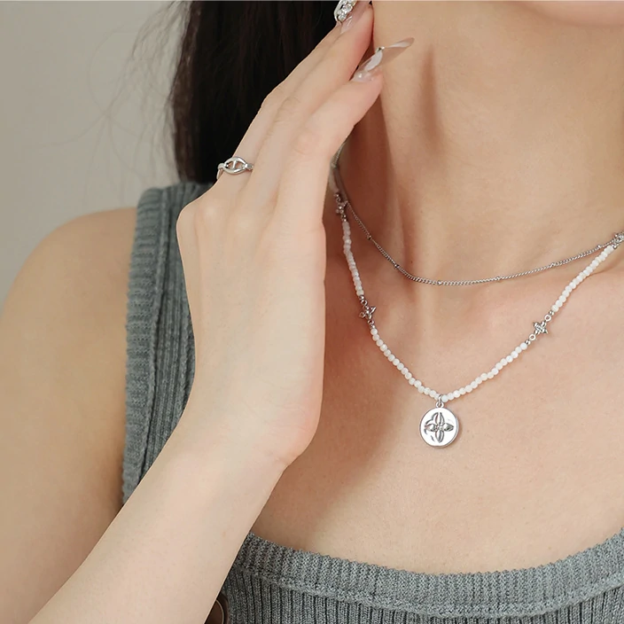 Woman wearing LIVKE shell bead necklace with floral pendant at beach sunset, showcasing boho chic jewelry for summer adventures