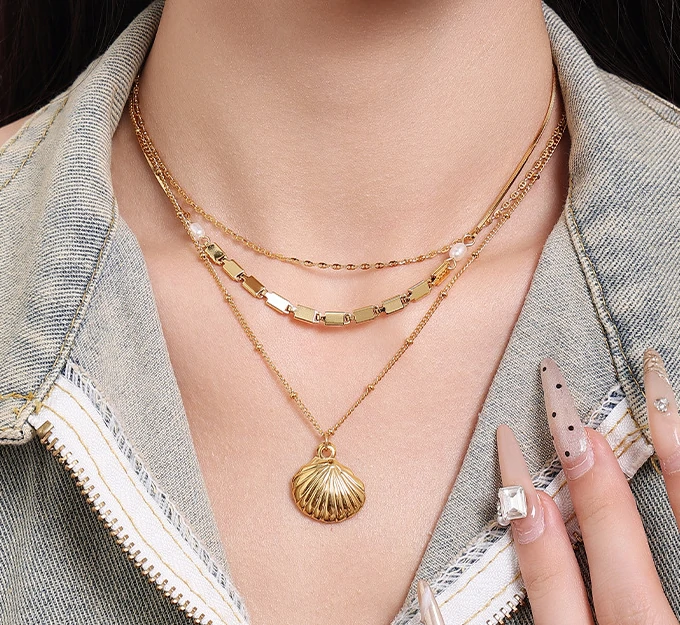 livke-tumbled-shell-necklace-california-beach Natural tumbled shell pendant on 18K gold-plated chain styled with linen shirt and jeans at beachside café